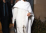 Meghan Markle in an all-white outfit with a flowing shirt, wide-leg trousers, and a dramatic cape, arriving at Paris Fashion Week.