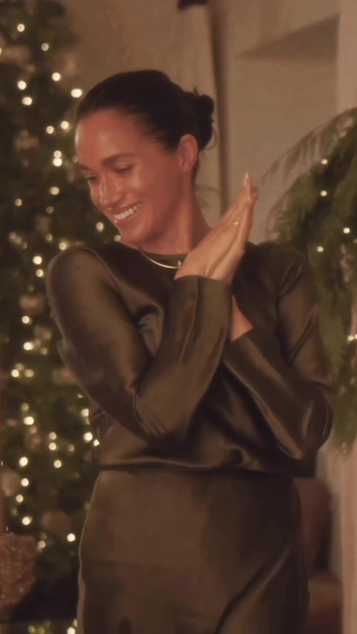 Meghan Markle smiling while wearing a dark green dress, with a Christmas tree in the background.